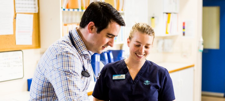 A medium close up shot of a male doctor showing a smiling, female nurse some paper work.
