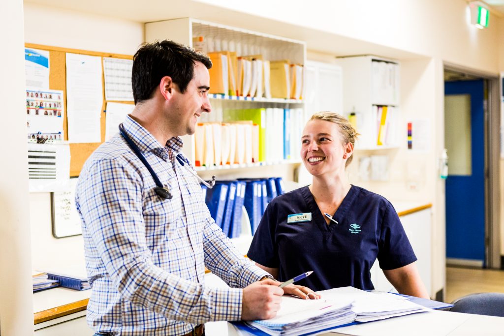 A medium close up shot of a male doctor and female nurse smiling at each other while filling out paper work.