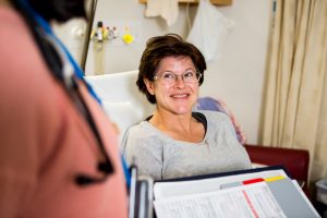 A close up of a female patient sitting up in bed, smiling.