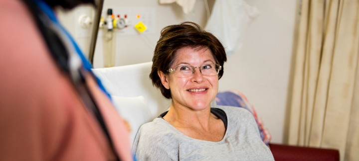 A close up of a female patient sitting up in bed, smiling.