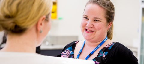 An over the shoulder photo of a woman wearing a Mercy Health lanyard smiling at another woman.