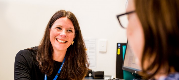 An over the shoulder photo of a woman wearing a lanyard smiling and holding a pen