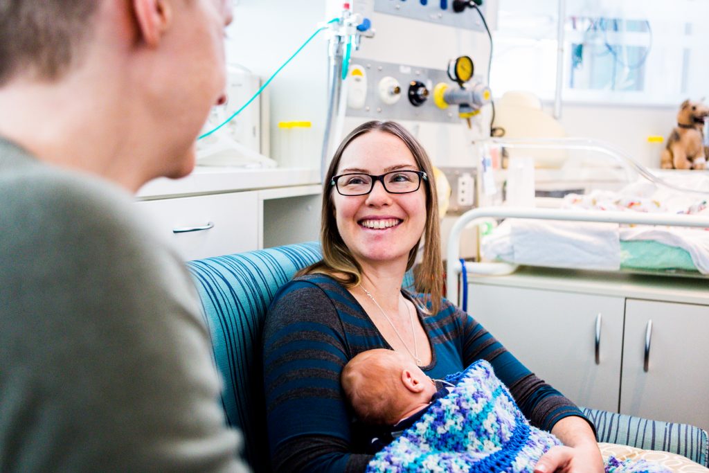 A young woman smiles while looking at her partner and holding a baby.