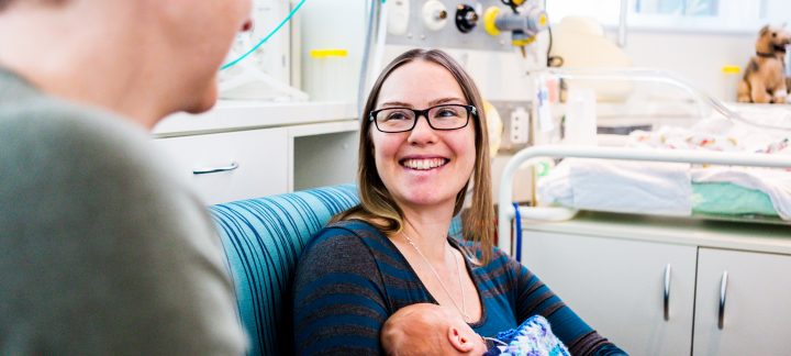 A young woman smiles while looking at her partner and holding a baby.