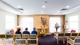Three elderly people sit in the front row of the hospital chapel.