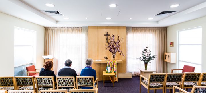 Three elderly people sit in the front row of the hospital chapel.