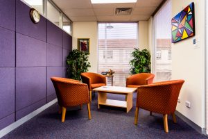 Four red arm chairs sit in a circle around a low coffee table next to a purple felt wall