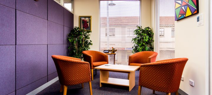 Four red arm chairs sit in a circle around a low coffee table next to a purple felt wall
