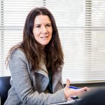 Close up of a woman holding a pen and clipboard, explaining something.