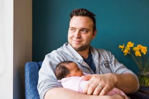 A man sits smiling out the window while holding a new born baby swaddled in pink